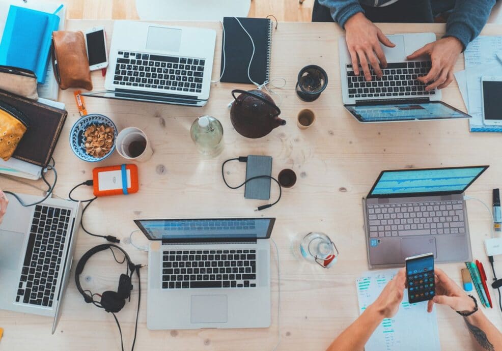 Vista cenital de una mesa de trabajo con varios portátiles, móviles y herramientas del equipo