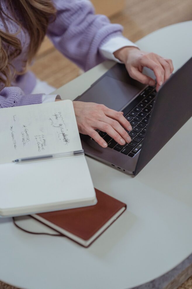 Persona redactando un artículo de blog en un portátil con un cuaderno de notas