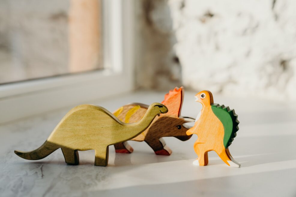 Dinosaurios de juguete de madera sobre una superficie clara junto a una ventana