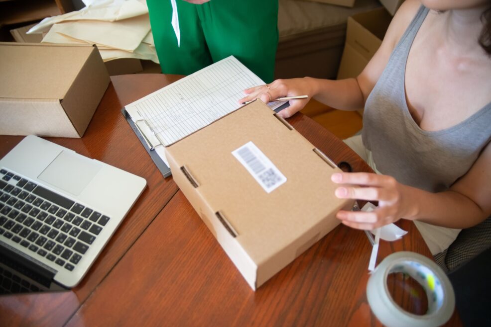 Manos preparando y precintando un pedido online junto a un portátil